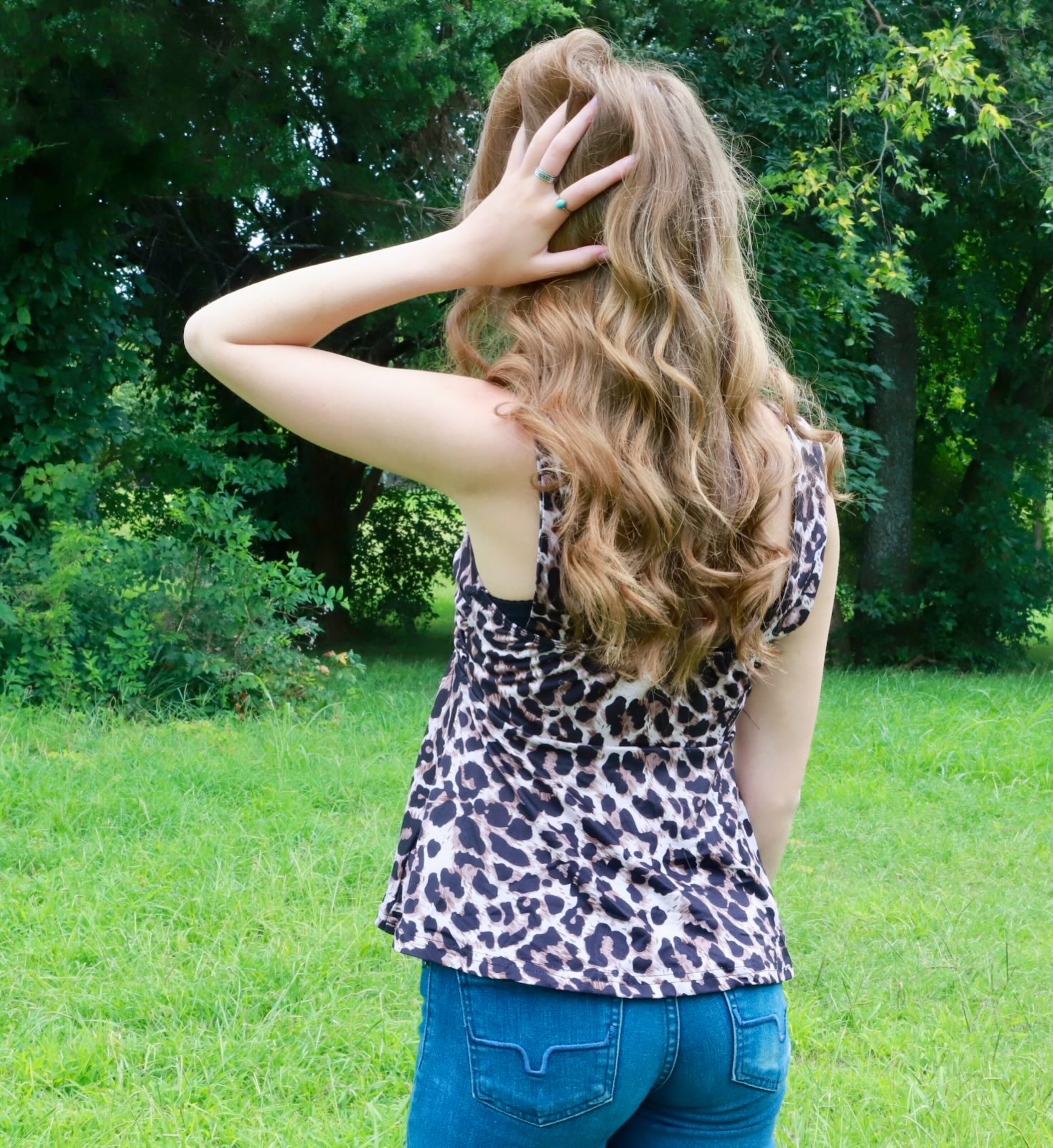 Portrait from behind in a grassy field, hand in long wavy hair.